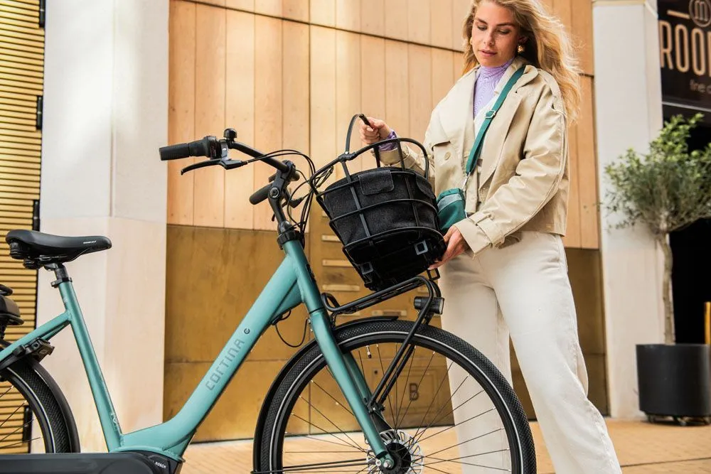 woman placing a bike basket on a cortina e-common electric women's bike